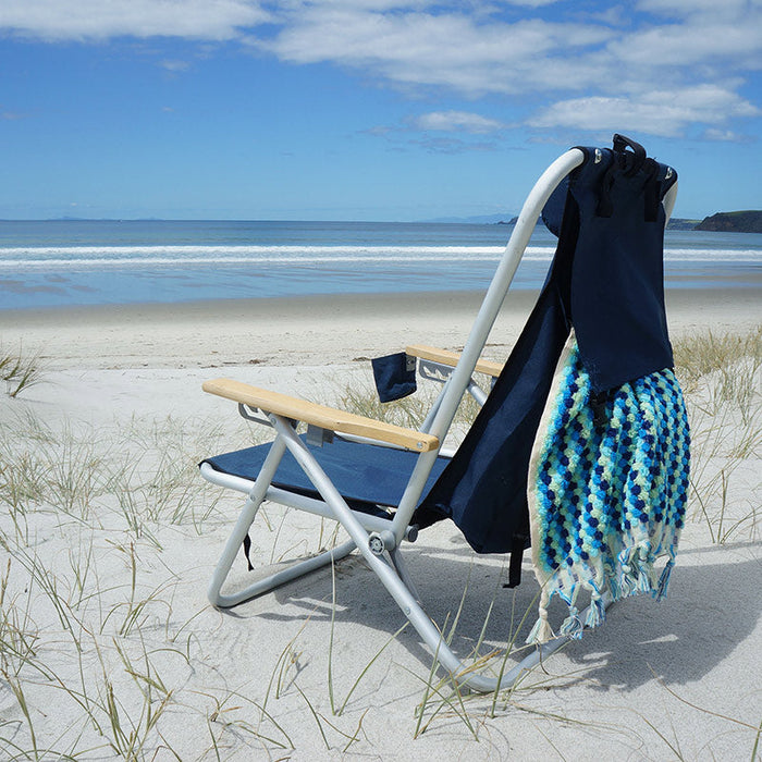 Beachkit Wearever Backpack Chair on sandy beach with ocean background and blue blanket hanging on chair