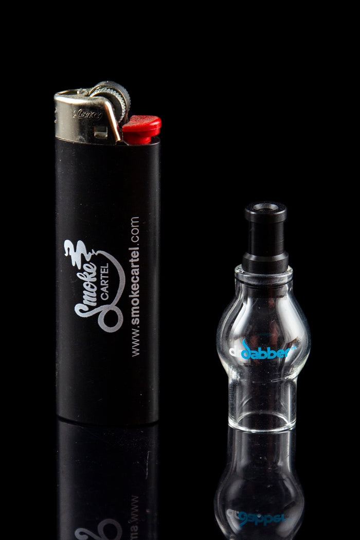 Black lighter with “Smoke Cartel” branding next to a clear glass dab rig on a reflective surface.