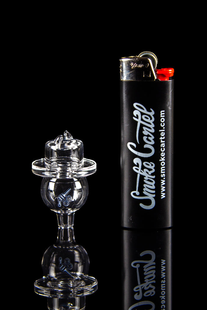 Close-up side view of the Honeybee Herb Quartz Dual Spinner Carb Cap resting beside a black lighter, shown on a reflective black surface.