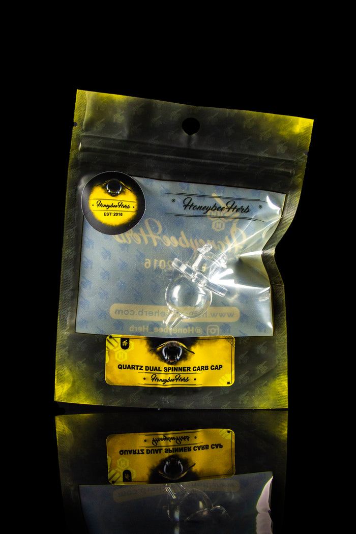 Angled close-up of the Honeybee Herb Quartz Dual Spinner Carb Cap in its clear blister pack against a black background.