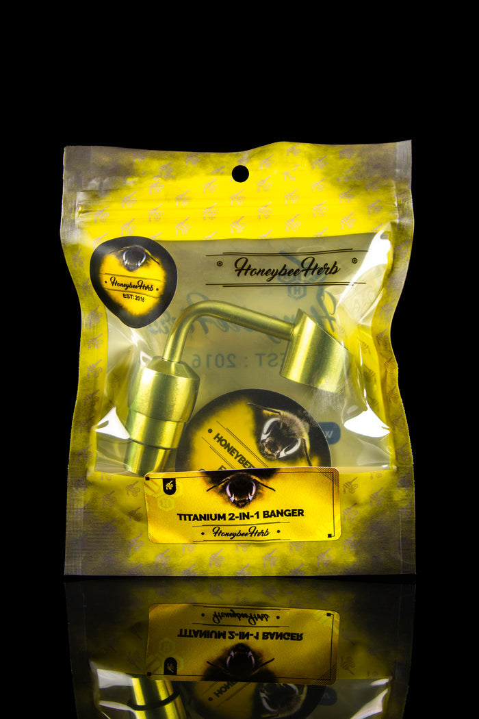 Top-down studio shot of the Honeybee Herb Titanium 2-In-1 Banger in yellow-backed packaging with the metallic banger visible through clear plastic.