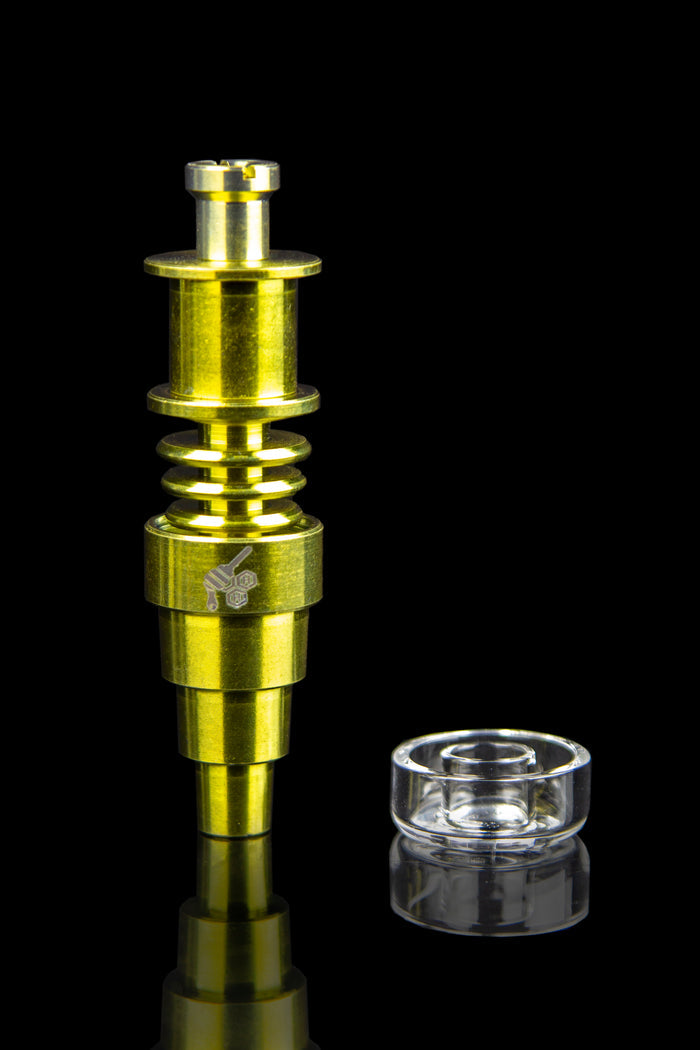 Gold-colored dab rig with a clear quartz insert, reflecting on a black surface.