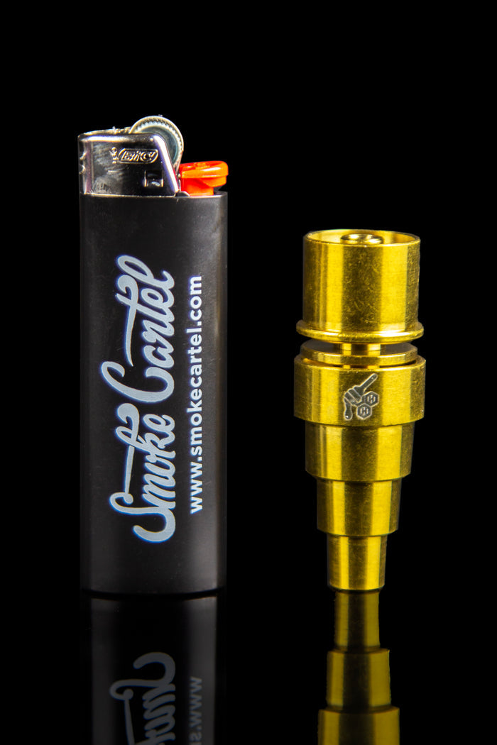 Gold titanium nail for dabbing cannabis concentrates beside a black lighter branded with “Smoke Cartel.”
