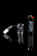 Glass dab rig with a quartz banger and butane torch, reflecting on a black glossy surface.