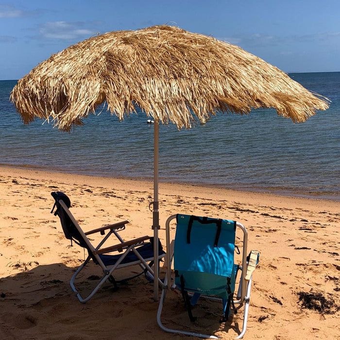 Hula 210cm beach umbrella with raffia thatch canopy providing UV 50+ sun protection on sandy beach with two chairs under shade