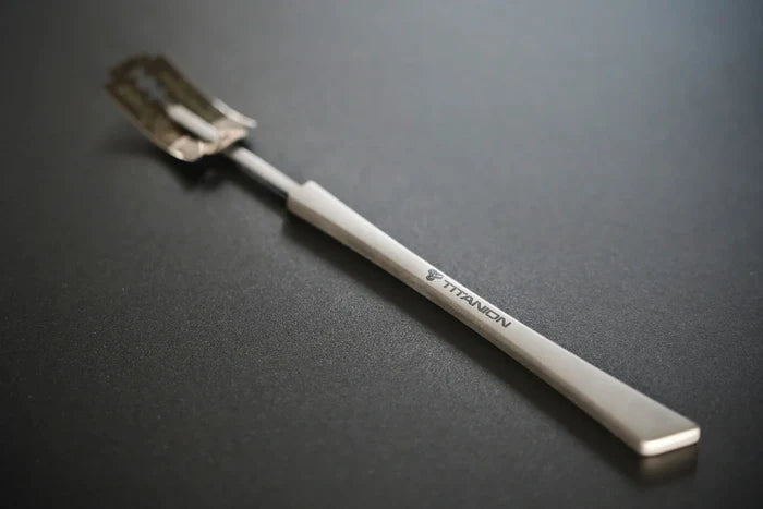 A close-up image of a titanium bread lame, showing its scoring blade and ergonomic handle.