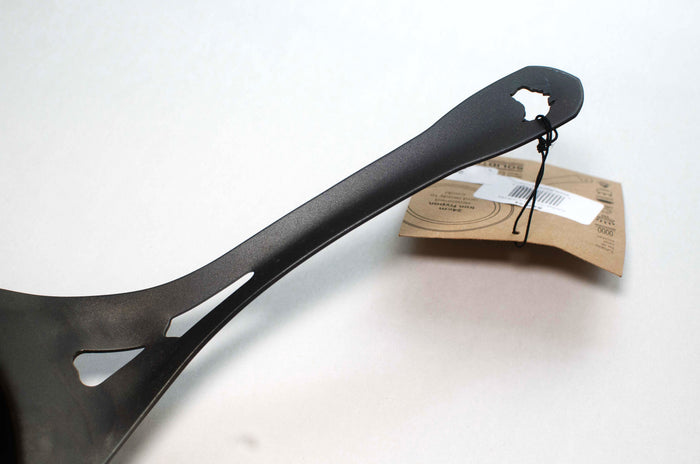 The handle of a 24cm seasoned carbon steel black fry pan on a white background with the tag looped through the Australia cut out in the handle.