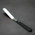 A 4 inch blade offset spatula with a black aluminum handle and a titanium blade, displayed on a dark textured surface.