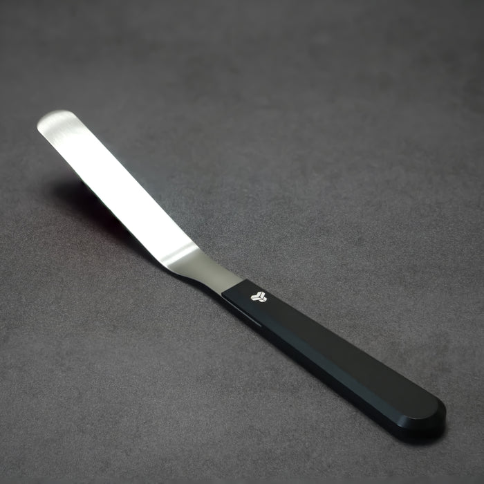 A 4 inch blade offset spatula with a black aluminum handle and a titanium blade, displayed on a dark textured surface.