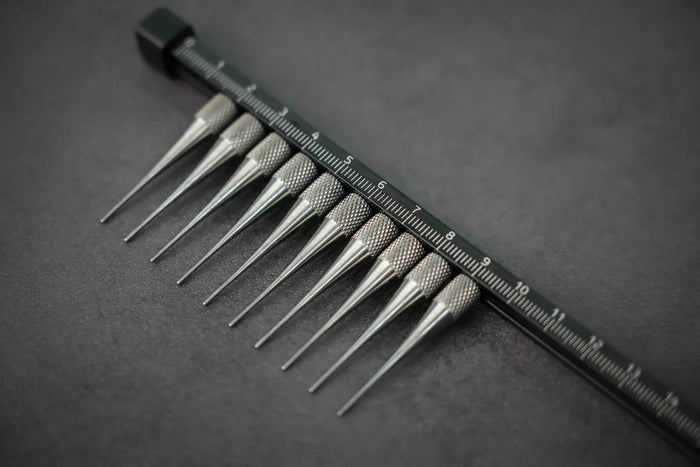 A close-up of a titanium glaze comb with 10 teeth, laid on a dark surface.