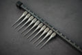 A close-up of a titanium glaze comb with 10 teeth, laid on a dark surface.