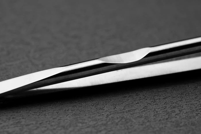 Close-up of a metallic tweezer on a dark textured surface.