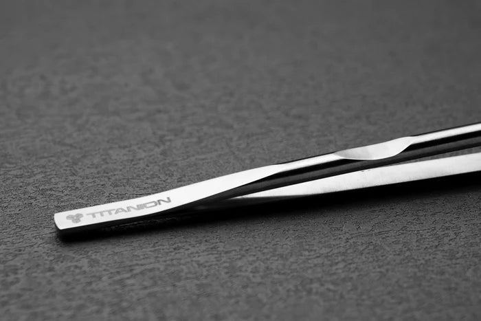 Metal tweezer with a brand logo on a dark surface
